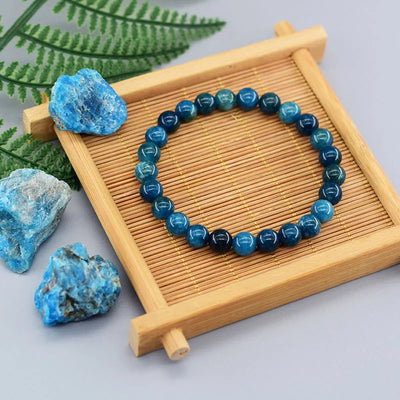 Pulsera de perlas de apatita azul sobre un soporte de de madera con piedras a la izquierda